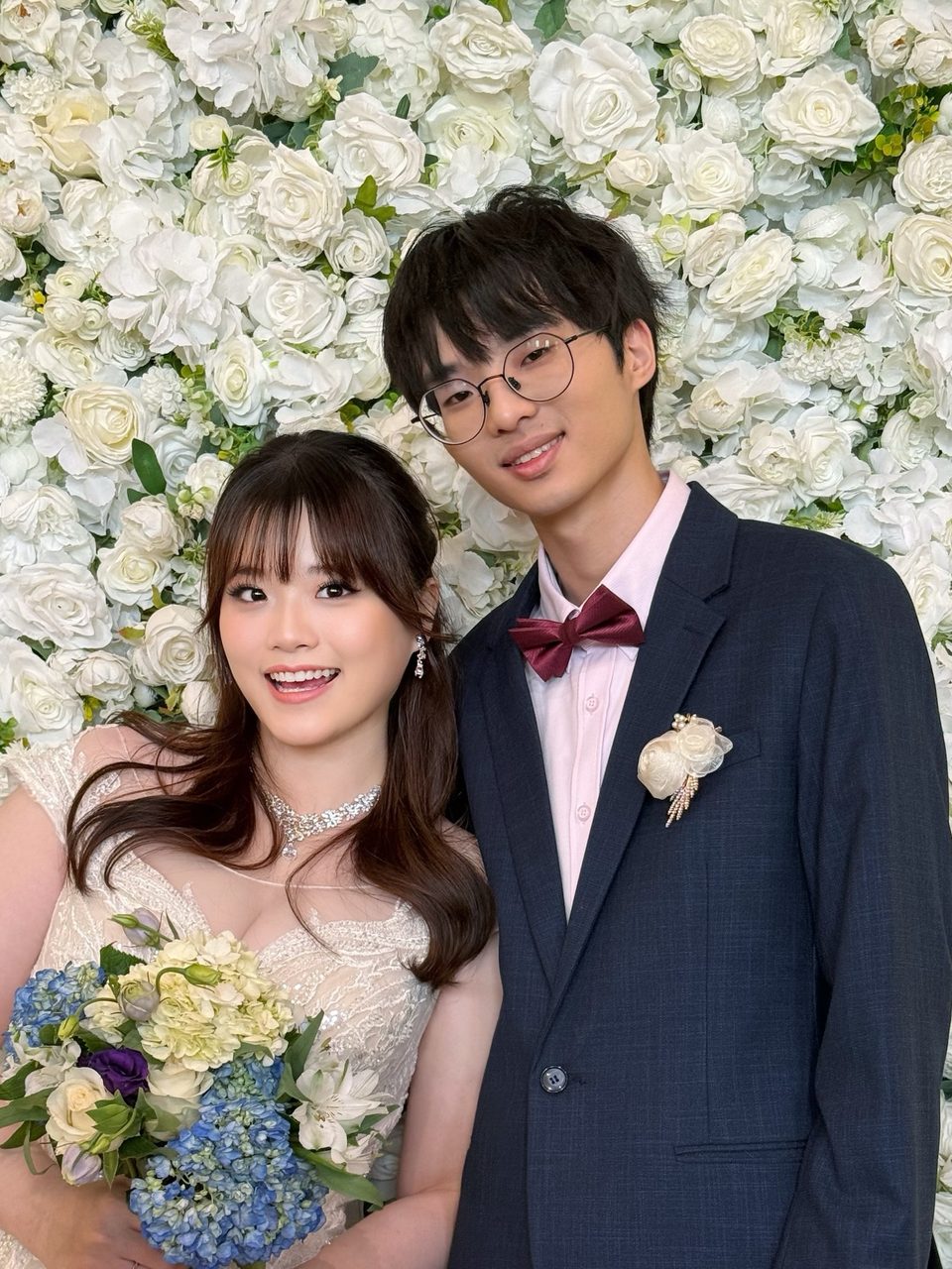 Bride and groom in front of a white flower wall